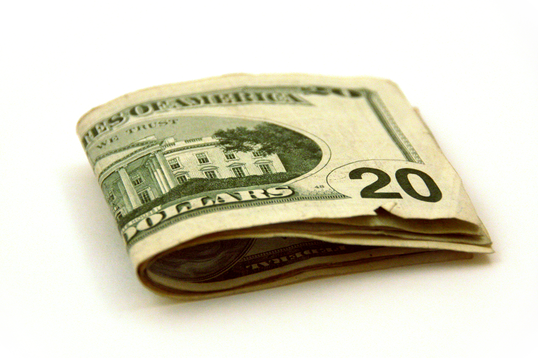 A folded twenty-dollar bill is isolated on a white background. The bill displays the White House on one side and features a slight curl, giving it a somewhat worn look.