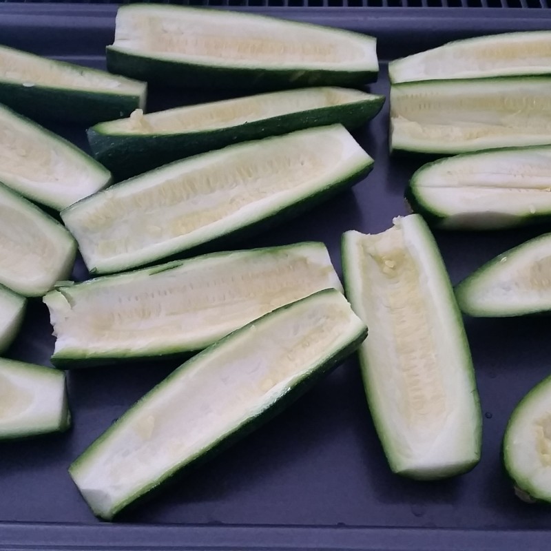 Halved and hollowed-out zucchinis are arranged on a baking tray, transforming into Zucchini Pizza Boats in preparation for stuffing.