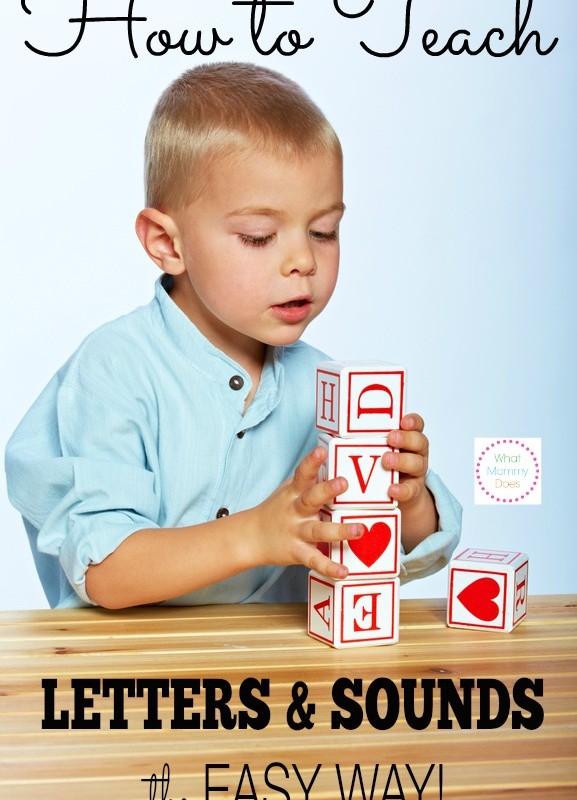 A young boy sits at a table with a serious expression, stacking wooden blocks featuring letters and symbols. The image is captioned "How to Teach Letters & Sounds the Easy Way!" The background is plain, and the boy is wearing a light blue shirt. Discover how to teach letters and sounds effortlessly!