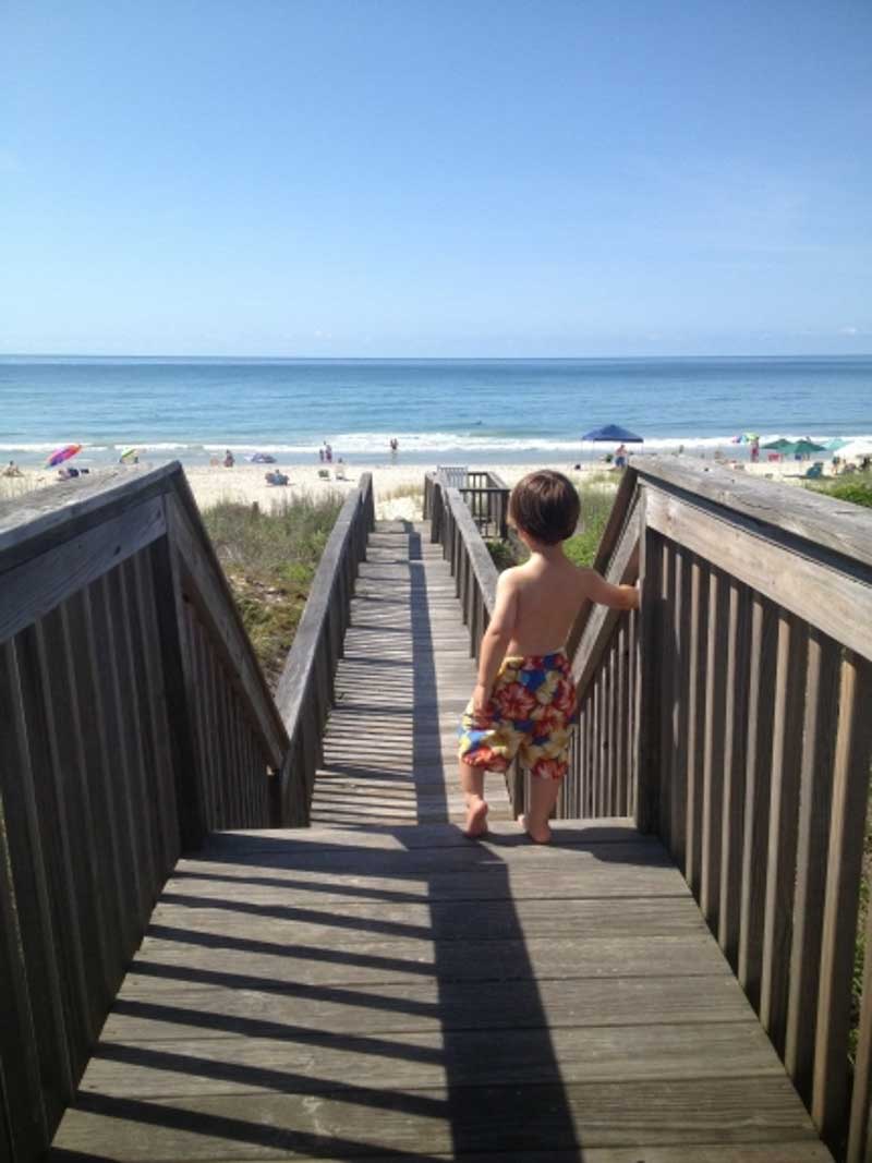boy standing on walkway towards ocean