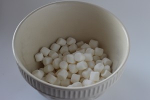 A white ceramic bowl filled with small, white mini marshmallows sits against a plain, light-colored background, evoking the simplicity of a ghostly Halloween treat.