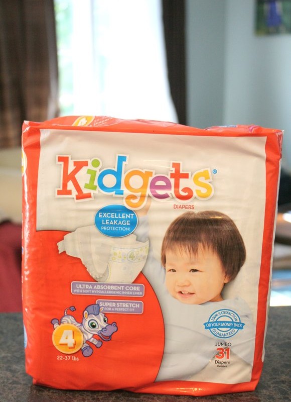 A package of Kidgets Value Diapers is shown on a countertop. The orange and white packaging, featuring an infant, boasts "Excellent Leakage Protection" and an "Ultra Absorbent Core." Available at Family Dollar, this pack contains size 4 diapers for babies weighing 22-37 lbs.