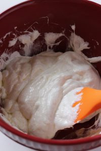 red mixing bowl with pumpkin spice rice krispie treats mixture inside. being mixed by a spatula.
