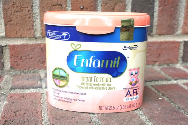 A container of Enfamil Infant Formula rests against a brick wall. The label indicates it is a milk-based powder with iron, thickened with added rice starch for infants up to 12 months to help reduce spit-up. The net weight is 21.5 oz (1.34 lb or 610 g). Perfect for those armed with savvy parenting tips!