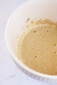 A white mixing bowl filled with light brown, frothy batter, perfect for an easy Christmas cookie recipe. The batter appears to have small bubbles, indicating it may be in the process of fermentation or rising. The bowl sits on a light marble surface.