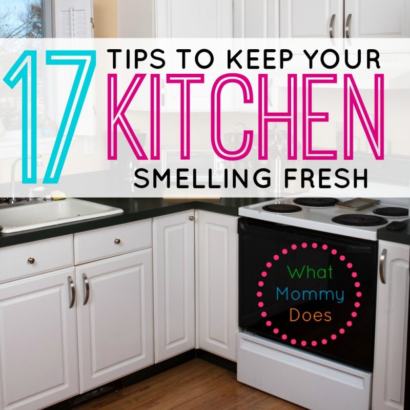 Image shows a modern kitchen with white cabinets and a black countertop. In the center of the image, overlaid text reads "17 Tips to Keep Your Kitchen Smelling Fresh," with "What Mommy Does" below that. The kitchen appears clean and well-organized, promising effective solutions for common kitchen smells.