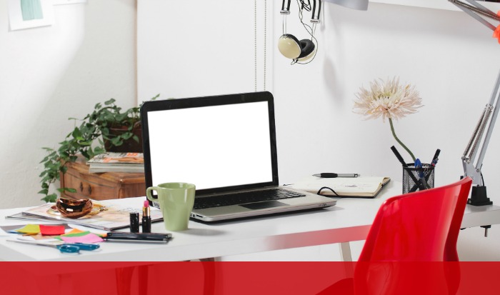 A modern white desk with a laptop, a green coffee mug, a stack of notebooks, colorful sticky notes, pens, and a plate with toast emphasizes productivity. A red chair sits in front of the desk. With a potted plant and flower in a vase on the desk and an overhead lamp, it’s time to make money blogging!