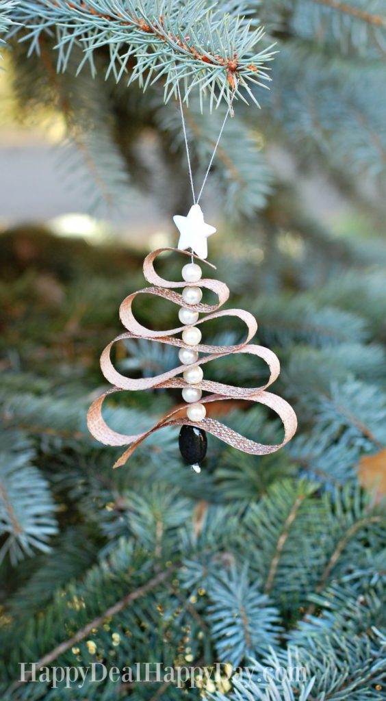 A handcrafted Christmas ornament shaped like a tree hangs on a pine branch. Made with loops of brown material, adorned with round white beads and a white star on top, it also features a black bead at the bottom. This unique decoration doubles as one of the perfect essential oil gift ideas.