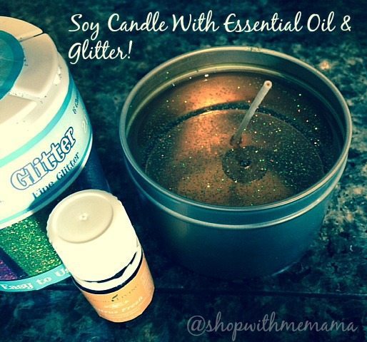 A soy candle tin surrounded by crafting supplies, including a container of fine glitter and a bottle of essential oil. The candle surface is speckled with glitter. Text at the top reads "Soy Candle With Essential Oil & Glitter!" Ideal for essential oil gift ideas. Follow @shopwithmemama!
