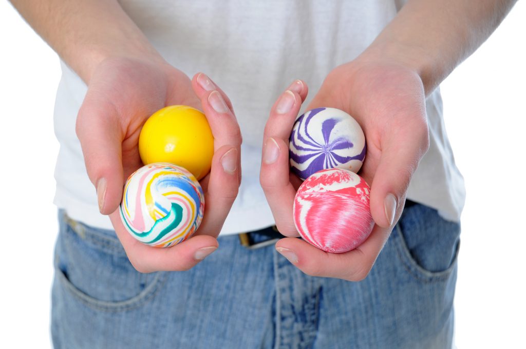 Hand holding a set of four round bouncy rubber balls with colorful designs on them