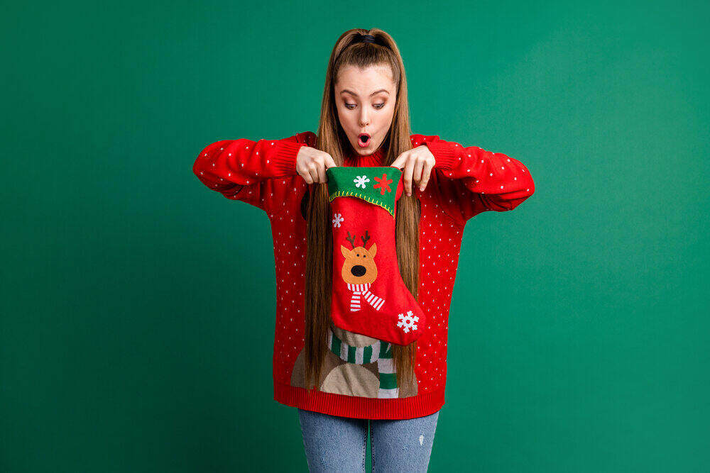 attractive young woman wearing a red sweater and looking shocked while holding a christmas stocking