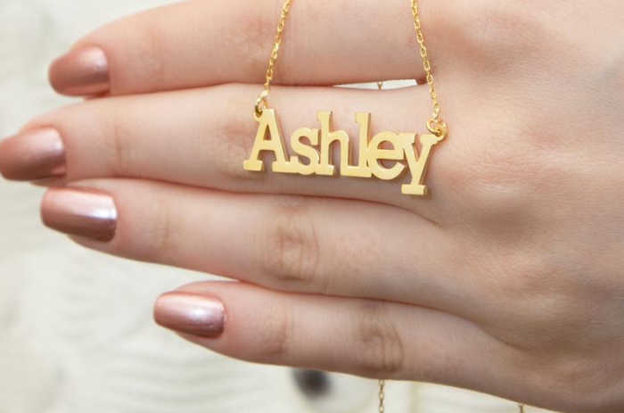 A gold necklace of the name Ashley. It is displayed on a hand. 
