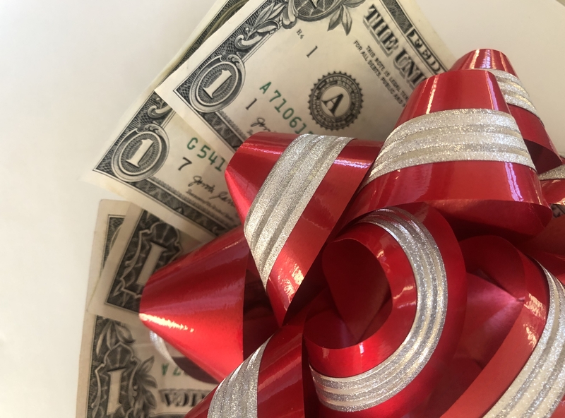 A close-up photo of two U.S. one-dollar bills partially tucked behind a shiny red and silver striped gift bow, placed on a white background, makes for a brilliant money gift perfect for any occasion.