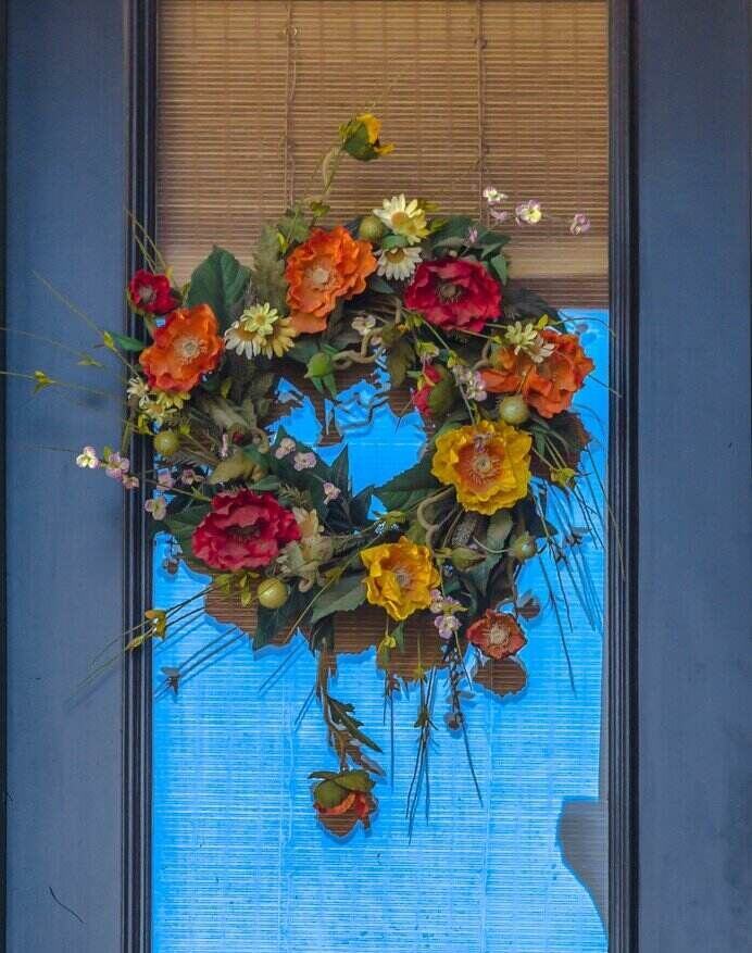 floral wreath on a door with orange, red and yellow flowers over a greenery.