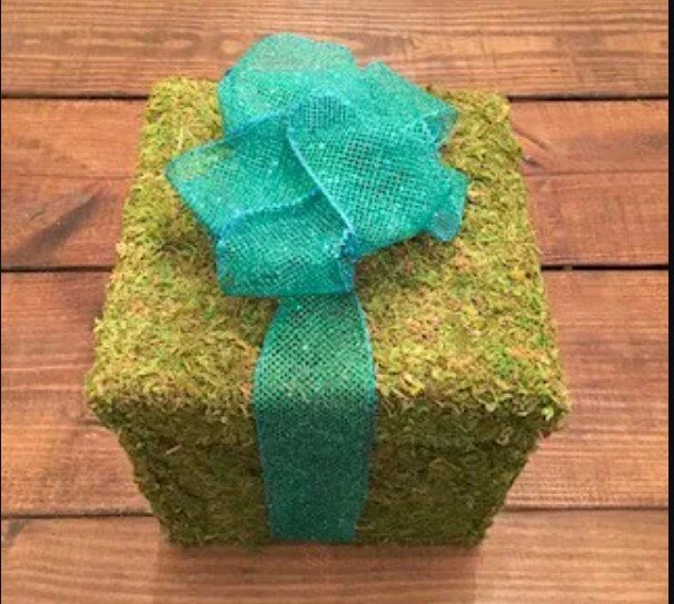 Box covered in green moss with a bigblue bow tied on it as a christmas decoration for a table.