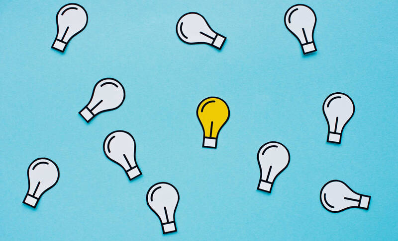 A blue background with multiple white light bulb illustrations scattered around, perfect for brainstorming Easy School Market Day ideas. Among them, there's one yellow light bulb illustration standing out from the rest.
