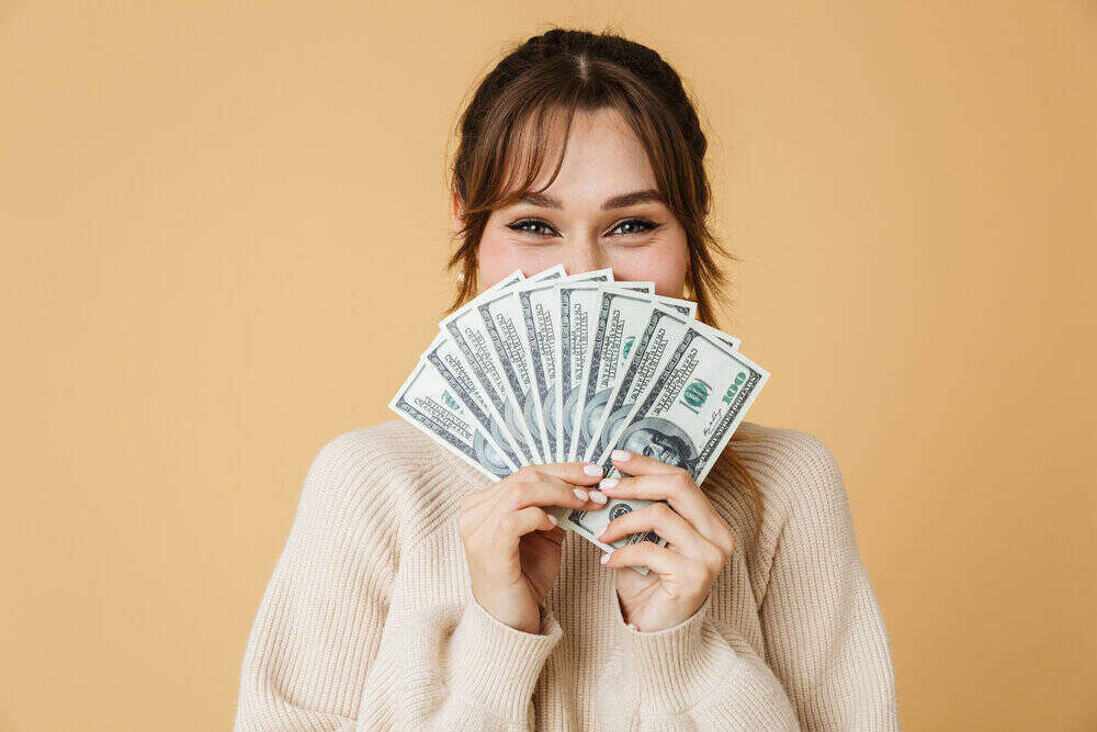 woman with brown hair holding money that is fanned out in front of her face. 