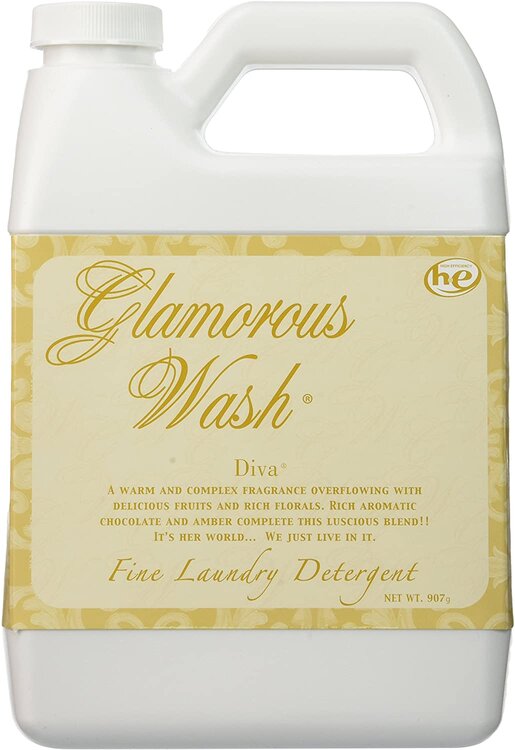 A rectangular, white plastic bottle of "Glamorous Wash" laundry detergent with a beige and gold label. The label features ornate text and decorative patterns. The bottle has a handle on top and holds 907g of detergent, ensuring your clothes stay clean and smell good after each wash.