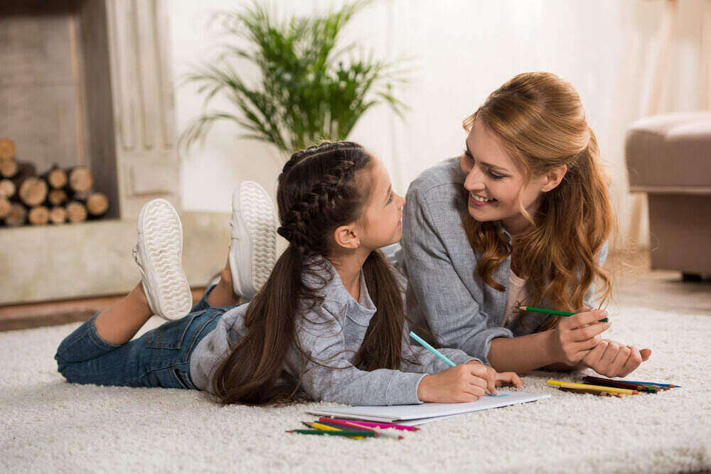 mother and daughter lying on a white carpet and coloring with pencils