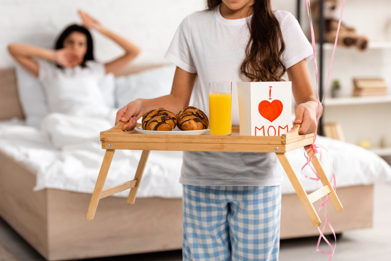 little kid serving her mom breakfast in bed as a gift