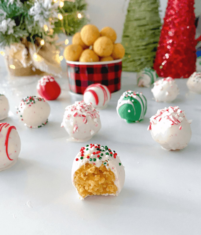 cake pop balls on a white table with assorted colors of icing and sprinkles