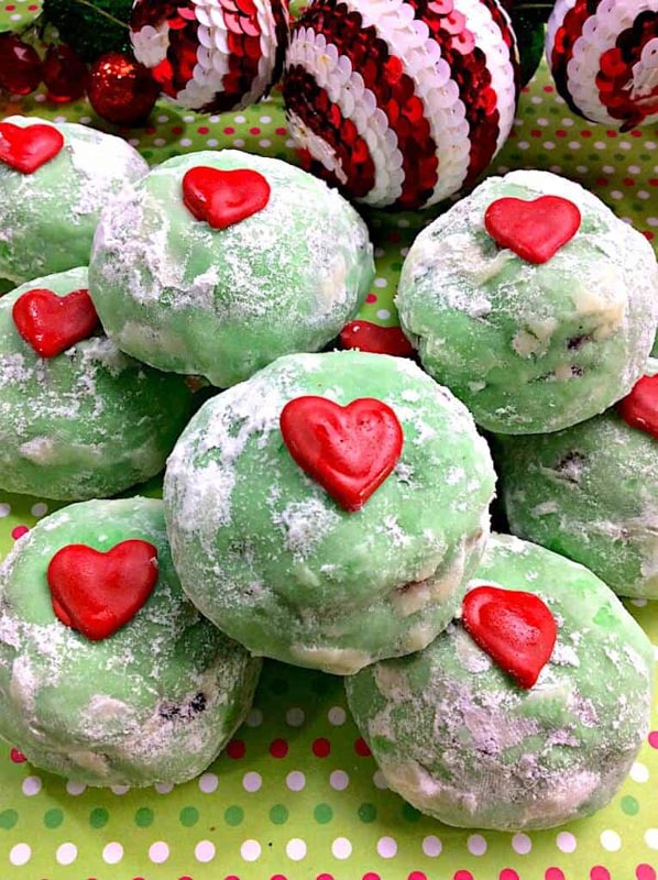 green colored snowball cookies with a small heart on the top of each in red icing