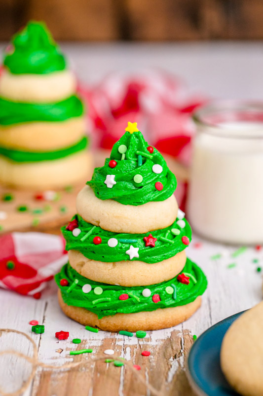 a stack of three sugar cookies with green icing and red and white sprinkles on top of each to look like a Christmas tree