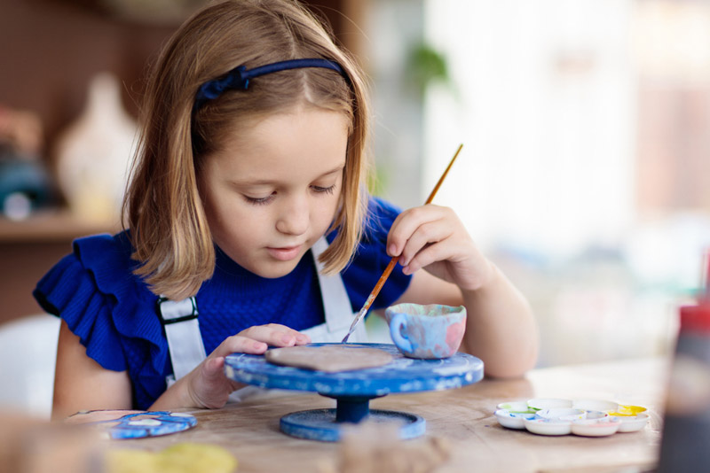 little girl painting a piece of pottery