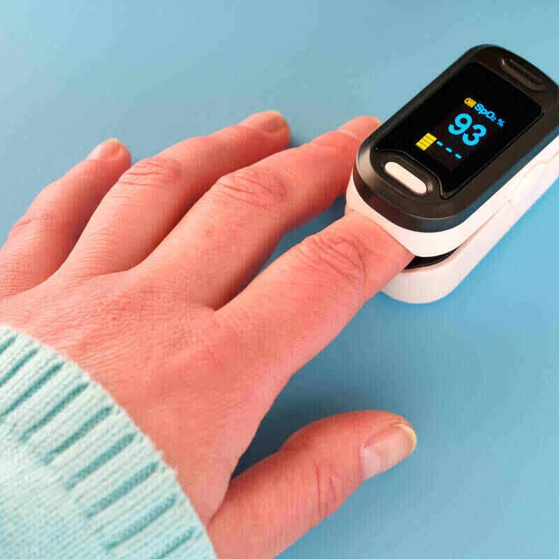 A hand with a light blue sleeve uses a pulse oximeter on the index finger. The item displays a reading of 93% oxygen saturation and a pulse rate of 74 beats per minute against a solid light blue background. This simple device has been critical in monitoring health, especially during Covid times.