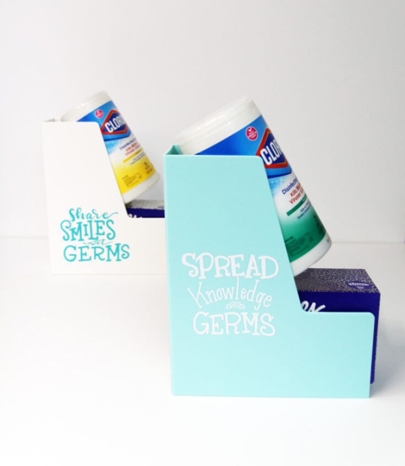 Two bookends on a white surface, each holding Clorox disinfecting wipes and a box of tissues. The left bookend is white and reads "Share SMILES NOT GERMS," while the right one is light blue and reads "SPREAD Knowledge NOT GERMS." Perfect for teacher gift basket ideas!