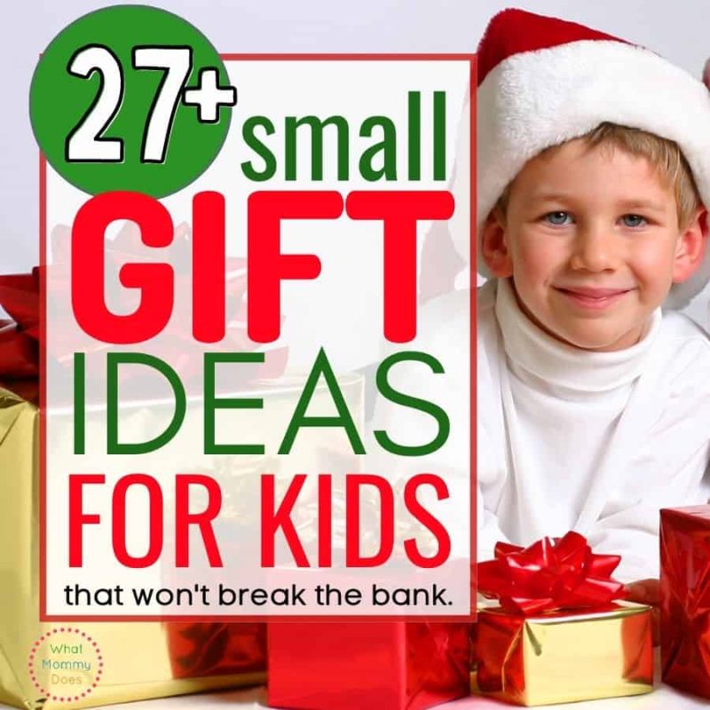A young child wearing a Santa hat and white shirt sits amid wrapped gifts. Text overlay reads, "27+ Small Gift Ideas for Kids that won't break the bank." The background includes red and yellow gift boxes with bows. The logo says, "What Mommy Does.