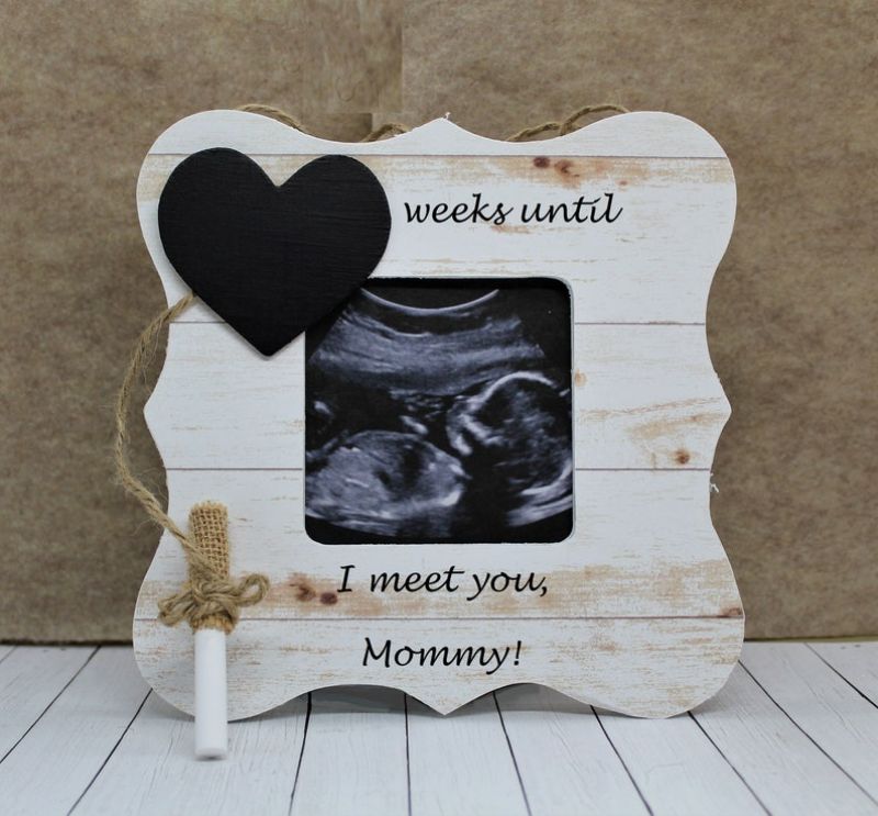 A rustic wooden picture frame with a black heart in the top left corner, displaying a black and white ultrasound image. Perfect for expecting mothers, the frame reads "___ weeks until I meet you, Mommy!" on the bottom and includes a small white chalk for writing. Ideal as Mother’s Day gifts.