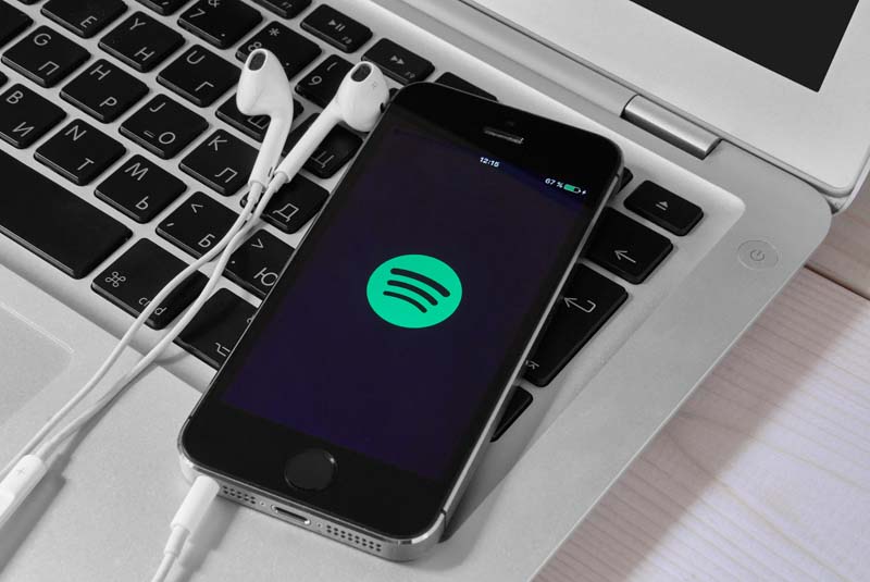 iphone with spotify app open and headphones laying nearby