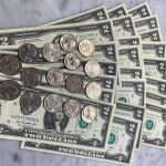 A stack of $2 bills and several quarters are arranged neatly on a marble surface, almost resembling a Money Pizza. The $2 bills are spread out in a fan-like manner, with the quarters aligned in two rows on top. This Simple Tutorial shows you how to make this creative display.