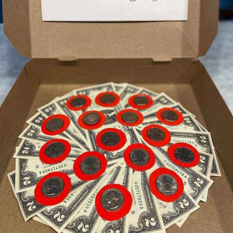 An open pizza box reveals an arrangement of dollar bills and coins laid out in a circular pattern to resemble a money pizza. A sign on the box's lid reads, "This may be, the best part of the pizza is the dough!" It's a simple tutorial on creativity with cash.