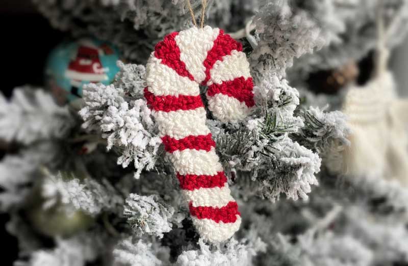 a candy cane punch needle craft ornament hanging on a tree