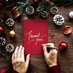 a person writing out the words thank you on a read Christmas card