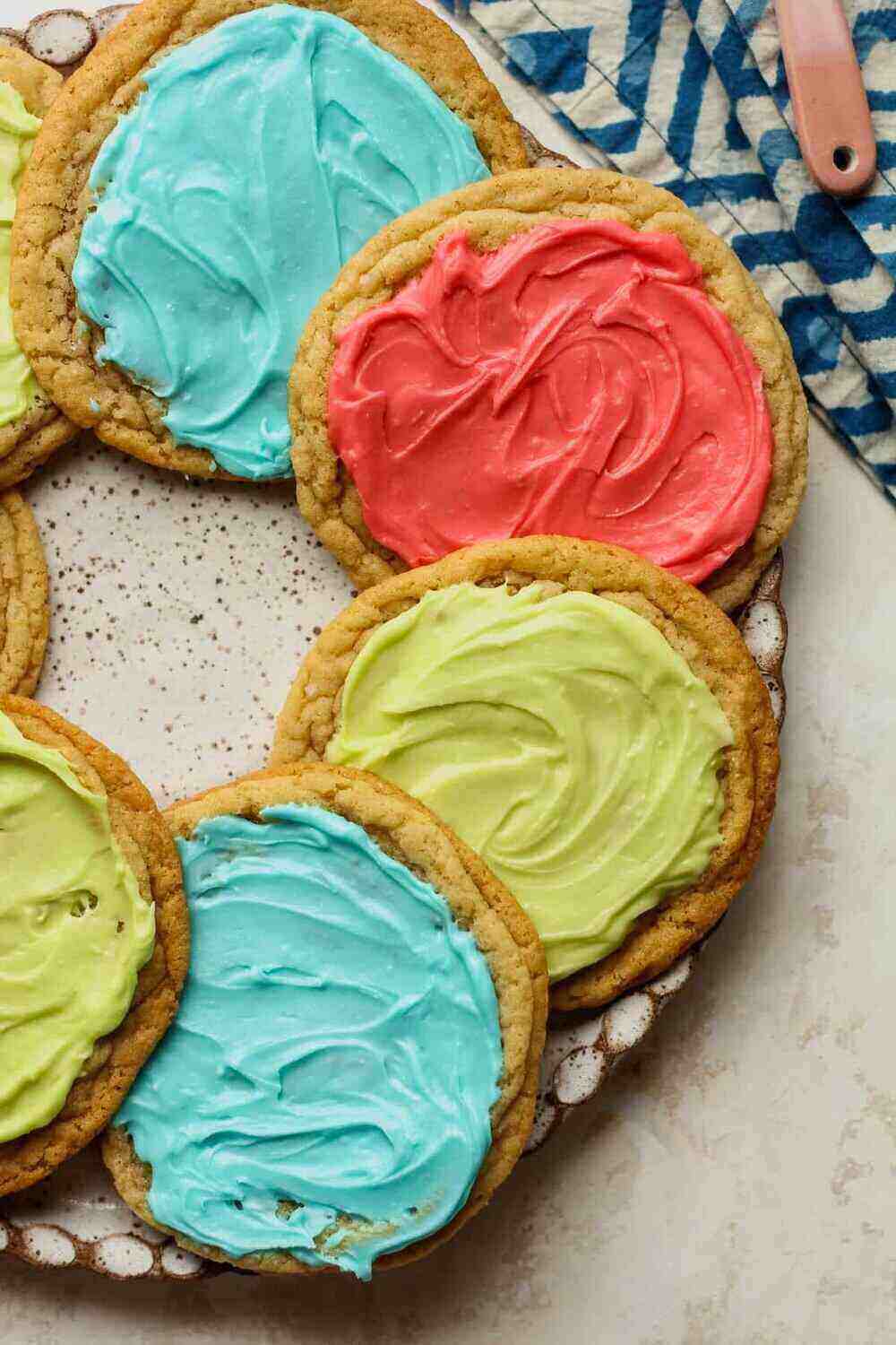 A plate of green, red and blue sugar cookies on top of a blue pattered tablecloth. These versatile cookies can be frosted for a summer bake sale or other holiday occasion!