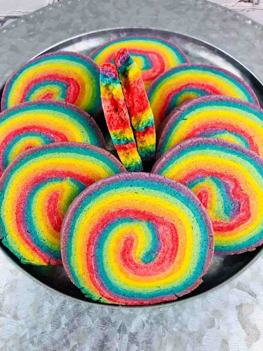 A plate of colorful cookies perfect for a summer bake sale. They are rainbow colored in a pinwheel pattern, a swirl of red, orange, yellow, green blue and purple. 