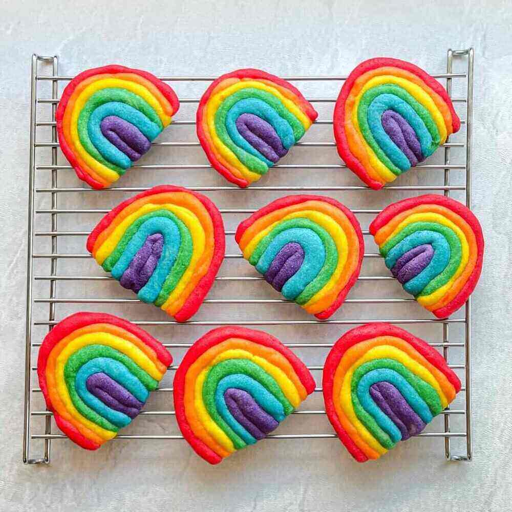 A photo of nine rainbow shaped and colored sugar cookies on a cooling rack. A delicious summer bake sale item!