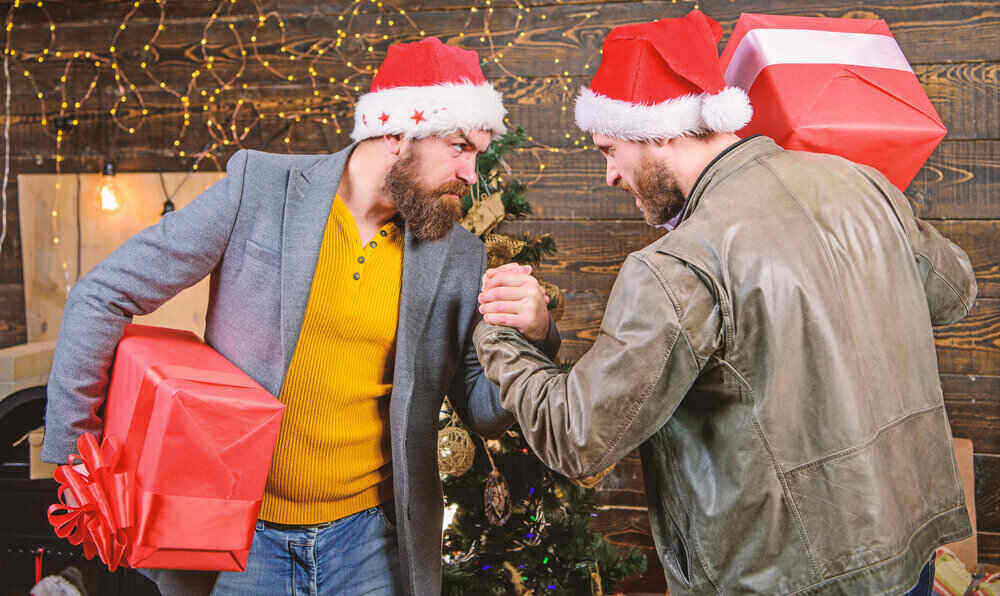 Two white men wearing santa hats and holding hands as if they are going to arm wrestle.
