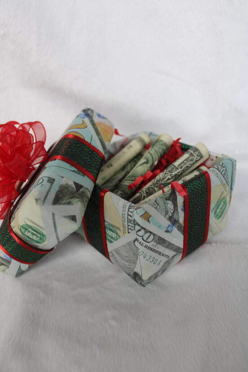 a box wrapped in money wrapping paper with a red bow on top that is filled with one dollar bills