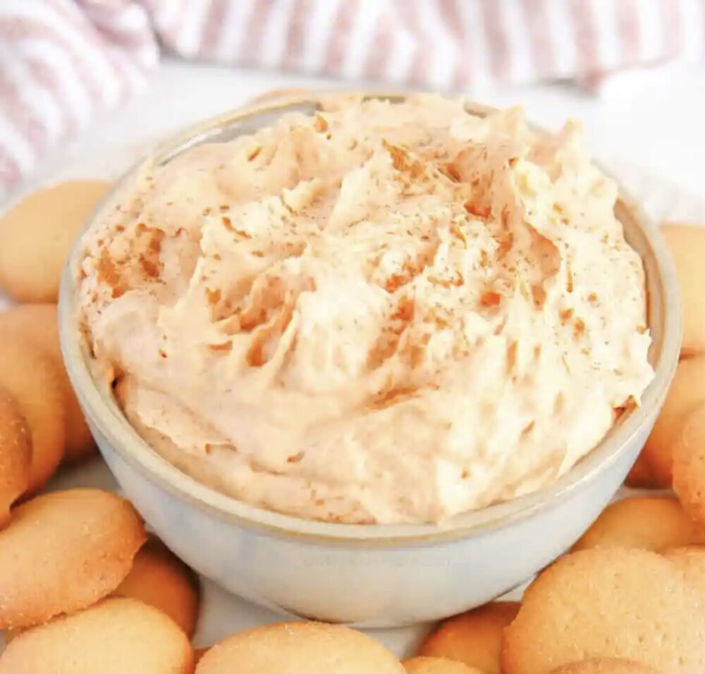 A white bowl full of pumpkin dip on top of a pile of vanilla wafers. 