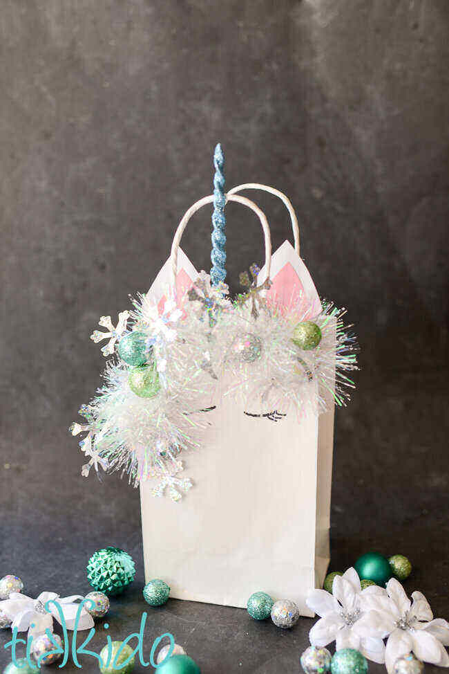 A gray background with a Christmas Unicorn Gift Bag. Blue ornaments are nearby.