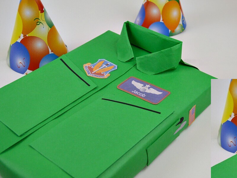 A green gift wrapped to look like an Air Force flight suit. Three party hats sit on the table nearby.