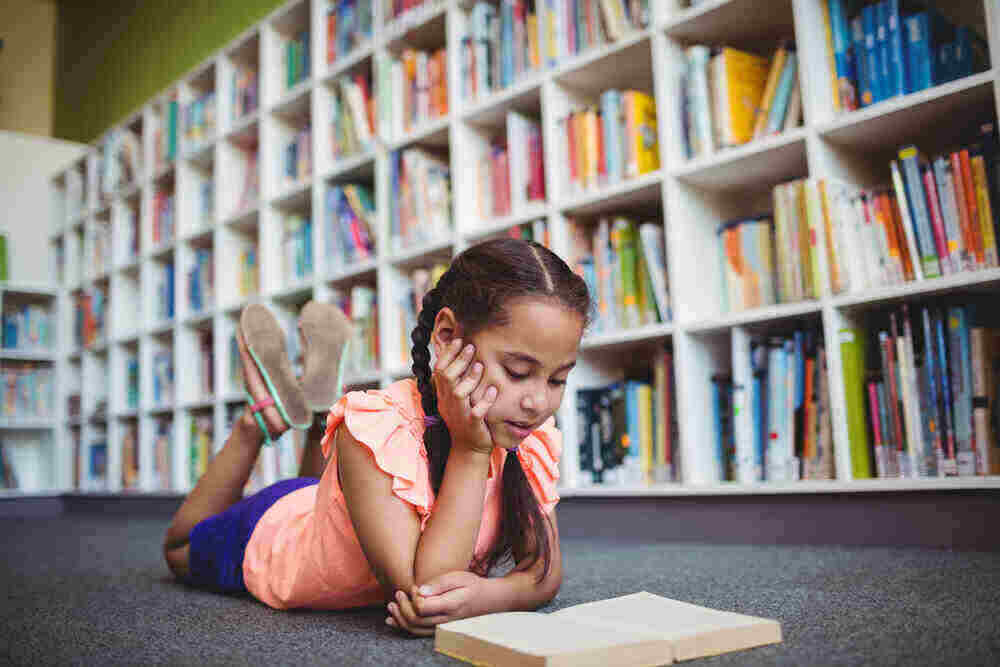 Girl lying and reading a book in the library