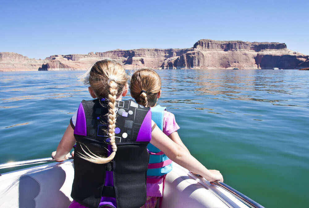 two girls wearing life jackets overlooking a lake with mountains in the background
