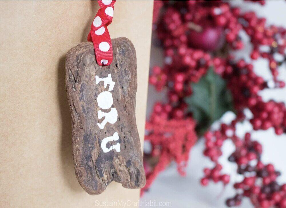 A brown package with a wooden tag hanging from a red polka dot ribbon. The tag is painted in white and says ForU.