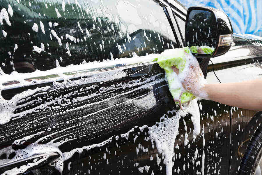 A hands hold a sponge while washing a car