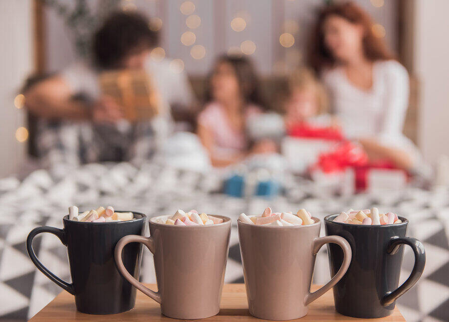 It's Christmas time! Four cup of hot cocoa with marshmallow on the table, family in bed in the background